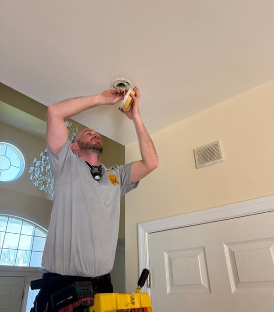 Ryan from Spartan Home Pros installing a combination smoke and carbon monoxide alarm on a ceiling