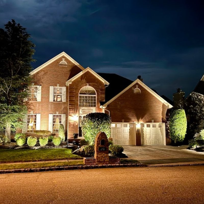 Brick home in New Jersey lit at night with landscape and outdoor lighting by Spartan Home Pros